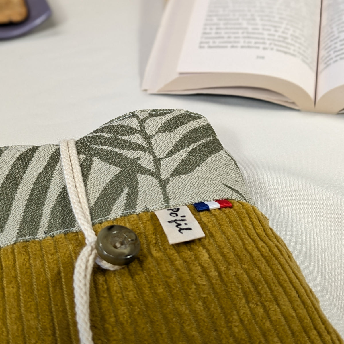 Zoom sur les finitions d'une pochette à livre de poche, velours côtelé jaune moutarde et tissu jacquard